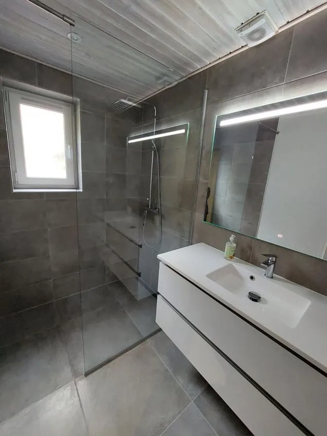 Renoveret badeværelse med glasvæg og hvide skabe